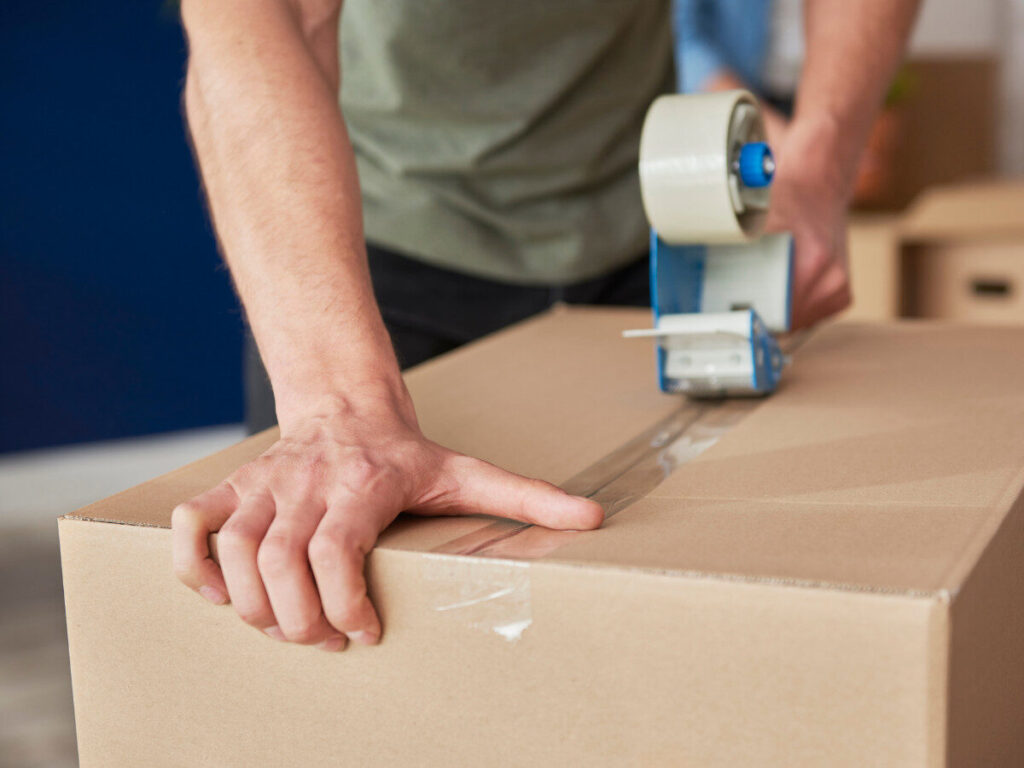 ダンボールにガムテープを貼る作業中の手元