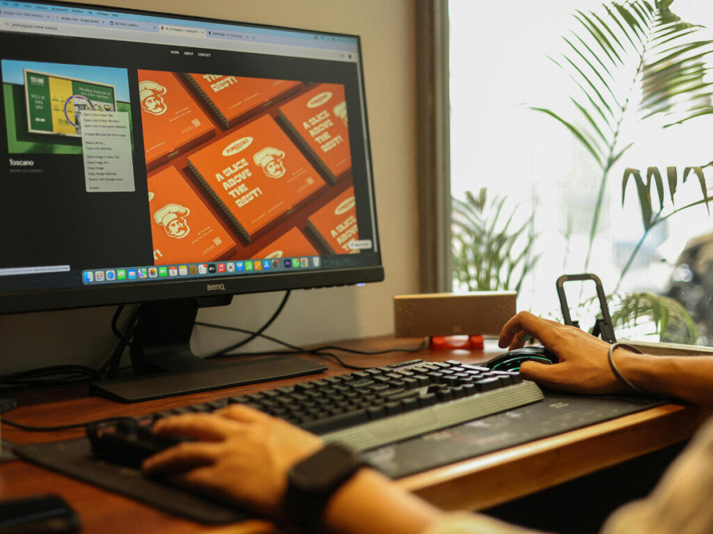 作業中の手元と大型モニターが映るデスク環境