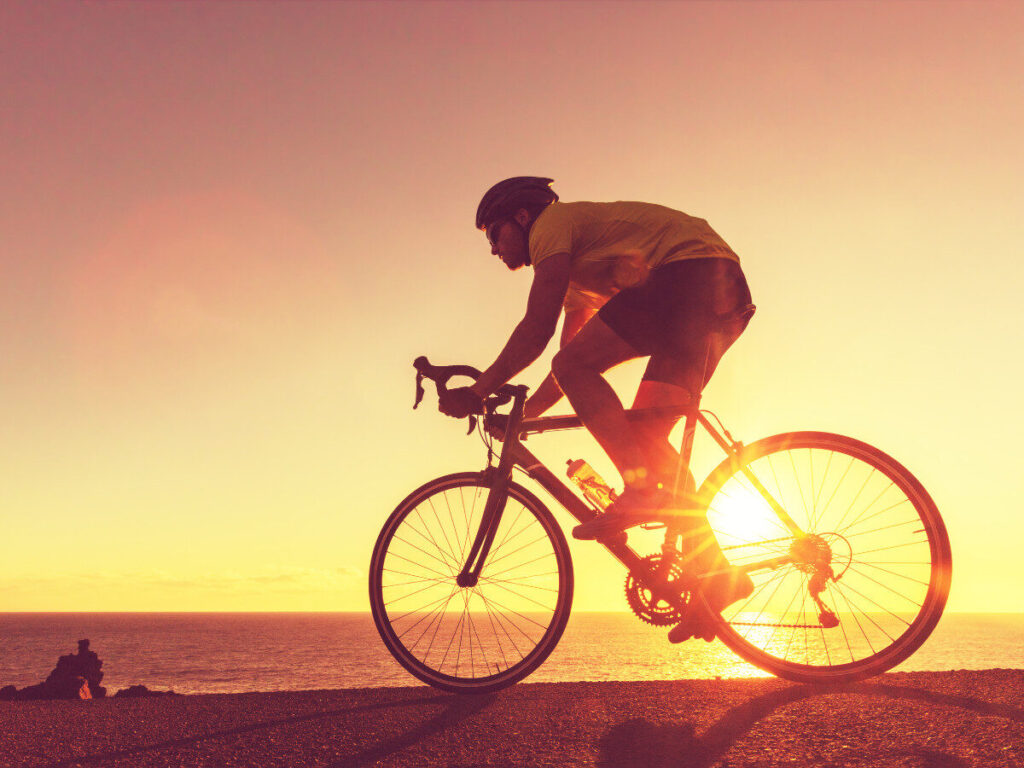夕焼け空の下を海沿いで走るサイクリスト